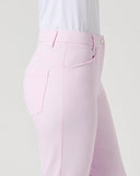 A close-up side view of a model wearing light pink tailored trousers and a white textured top against a plain light gray studio background.