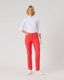 A woman modeling bright coral-red slim-fit pants with a white long-sleeve polo shirt and white gloves, standing against a light gray studio background.
