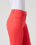 A close-up side view of a model wearing bright coral-red fitted pants with a white top, shown against a clean light gray studio background.