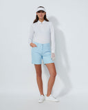 Woman wearing a white golf shirt, light blue shorts, and white shoes on a white background