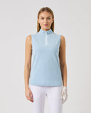 Woman wearing a light blue sleeveless top and white pants on a plain background