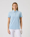 Woman wearing a light blue polo shirt and white pants on a plain background