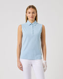 Woman wearing a light blue sleeveless polo shirt and white pants on a gray background