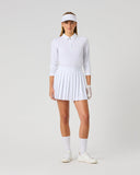 A woman modeling a white long-sleeve polo shirt, pleated tennis skirt, white visor, white gloves, white socks, and white sneakers against a light gray studio background.