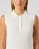 A woman wearing a sleeveless white polo shirt with a textured cable-knit pattern, shown from the chest up against a light gray studio background.