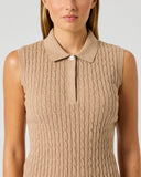A woman wearing a sleeveless knit polo shirt in a warm beige or camel color, shown from the nose down against a light gray studio background.