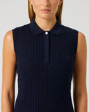 A woman wearing a sleeveless navy blue cable-knit polo top with a collar and a single button, shown against a plain light gray studio background.