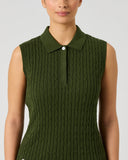 A woman wearing a sleeveless olive green polo shirt with a cable-knit texture, shown from the chest up against a light gray studio background.