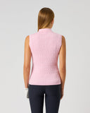 A woman viewed from the back wearing a sleeveless pink knit mock-neck top and dark navy leggings, standing against a light gray studio background.