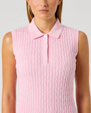 A woman wearing a sleeveless pink knit polo shirt with a cable pattern, shown from the chest up against a light gray studio background.