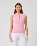 Woman wearing a pink sleeveless polo shirt and white pants on a light gray background