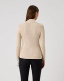 Woman wearing a beige sweater and black pants on a light gray background