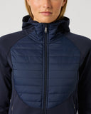 A woman wearing a navy blue hooded jacket with a quilted front panel and smooth sleeves, shown from the nose down against a light gray studio background.