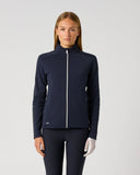 A woman modeling a dark navy blue athletic zip-up jacket with a high collar and white zipper, paired with matching dark pants, against a light gray studio background.