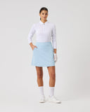 Woman wearing a white shirt, light blue skirt, and white shoes on a plain background