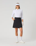 A woman modeling a white long-sleeve polo shirt, black skirt, white visor, white gloves, white socks, and white sneakers against a light gray studio background.