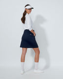 Woman wearing a navy skirt, white shirt, and visor on a light gray background