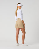 A woman modeling a white long-sleeve golf shirt, beige golf shorts, a white visor, and white sneakers, shown from a side-back angle against a light gray studio background.