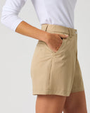 A person wearing beige high-waisted shorts with a white long-sleeve top, shown from the chest down against a light gray studio background.