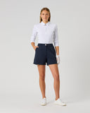 A woman modeling a white long-sleeve polo shirt and navy blue golf shorts, standing against a light gray studio background.