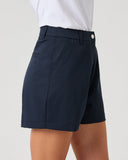 A person wearing navy blue tailored shorts with a white top, shown from the waist down against a plain light gray studio background.