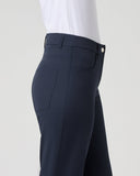 A side profile view of a person wearing navy blue tailored trousers and a white top, shown against a plain light gray studio background.