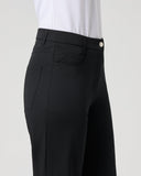 A close-up side view of a model wearing black high-waisted trousers and a white top, shown against a light gray studio background.