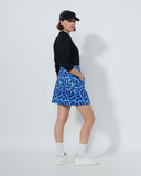 Person wearing a black jacket, blue patterned skirt, and white shoes on a white background