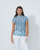 Woman wearing a floral blouse and white pants against a plain background