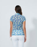 Woman wearing a blue patterned shirt and white pants on a gray background