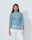 Woman wearing a blue floral patterned shirt and white pants on a plain background