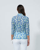 Woman wearing a blue floral blouse and white pants on a gray background