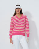 Woman wearing a pink patterned sweater and white pants on a plain background