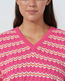 Woman wearing a pink and orange striped sweater against a plain background