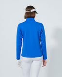 Woman wearing a blue long-sleeve top and white pants on a light gray background