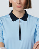 Person wearing a light blue polo shirt with a black collar and zipper on a plain background