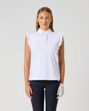 A woman modeling a white sleeveless collared golf polo shirt with ruffled shoulders and a white golf glove, paired with dark pants, against a light gray studio background.