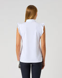 A woman viewed from the back wearing a white sleeveless collared top with ruffled shoulder details and dark pants, standing against a light gray studio background.