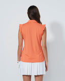 Woman wearing an orange sleeveless top and white pleated skirt on a plain background