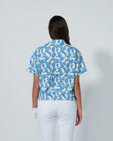 Person wearing a blue patterned shirt and white pants on a gray background