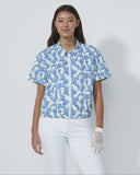 Woman wearing a blue and white patterned shirt with white pants on a plain background