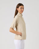 Woman wearing a beige shirt and white pants on a light gray background