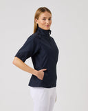Woman wearing a navy blue top and white pants on a light gray background