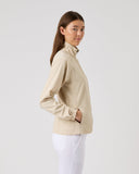 Woman wearing a beige blouse and white pants against a light gray background