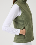 Person wearing a green quilted vest over a white long-sleeve shirt on a light gray background