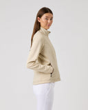 Woman wearing a beige jacket and white pants on a light gray background