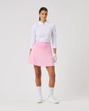 Woman wearing a white shirt, pink skirt, and white shoes on a light gray background