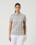 Woman wearing a patterned polo shirt and white pants on a plain background