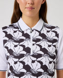 Person wearing a black and white floral patterned polo shirt on a plain background