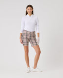 Woman wearing a white polo shirt and plaid shorts on a light gray background